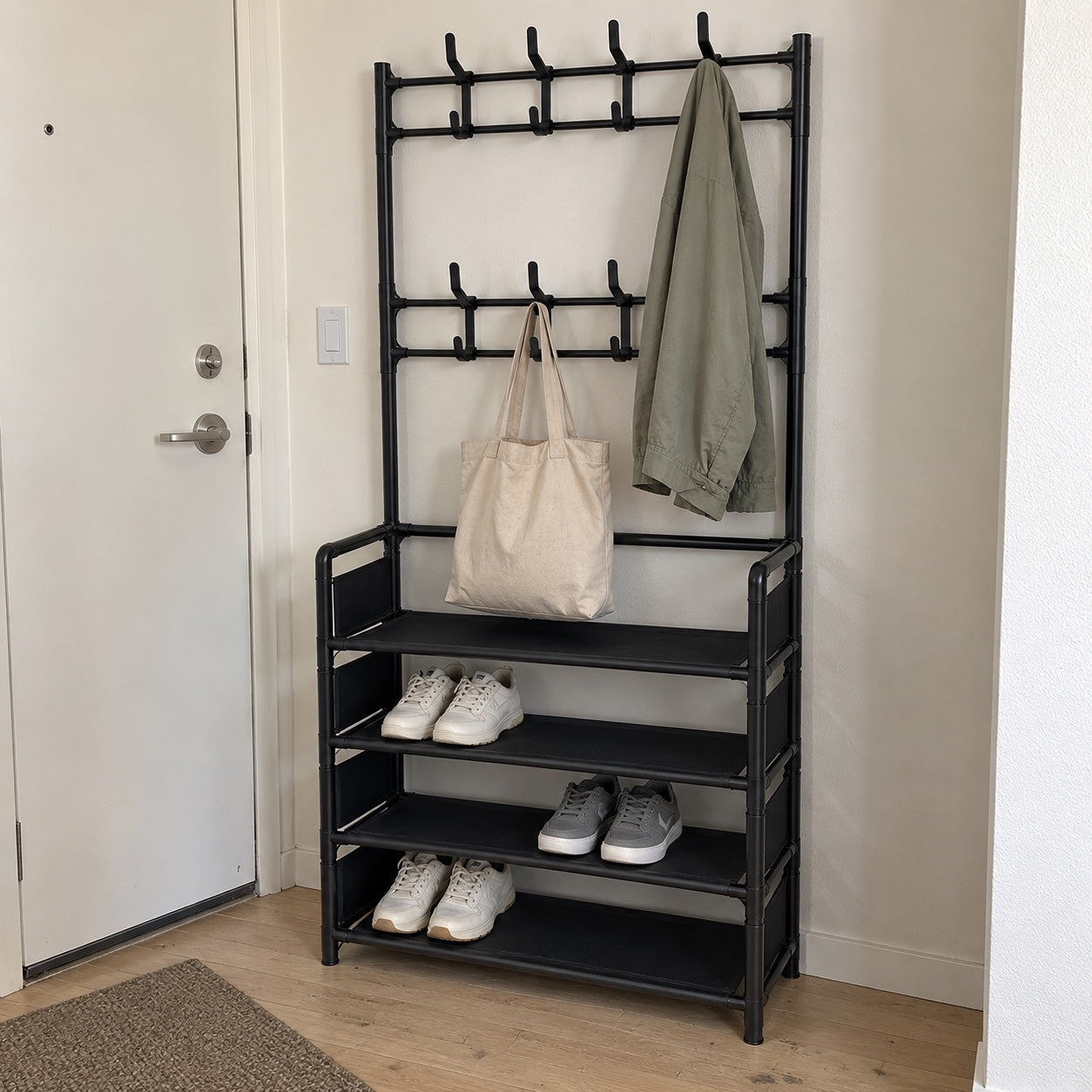the black rack beside an apartment entrance door, with a light olive jacket, beige canvas tote and everyday sneakers.
