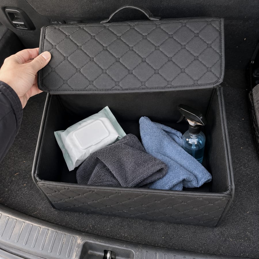 Open black organizer holding cleaning supplies, viewed from above in a car trunk.