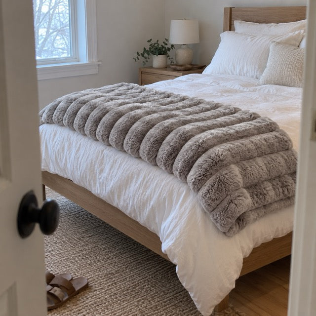 Customer photo: the Light Grey throw folded at the foot of a bed, viewed through a doorway.
