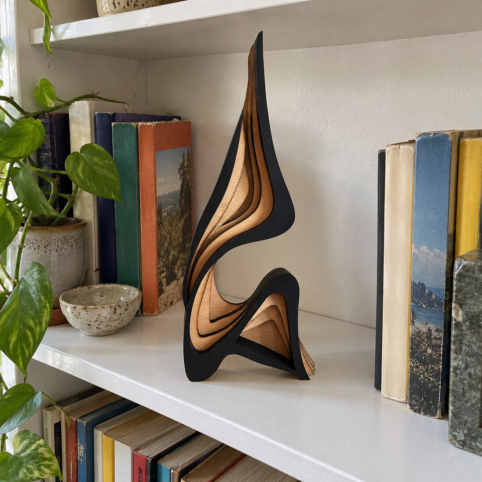 Small sculpture on a narrow white-painted bookshelf with ordinary colorful paperbacks, seen slightly from above.