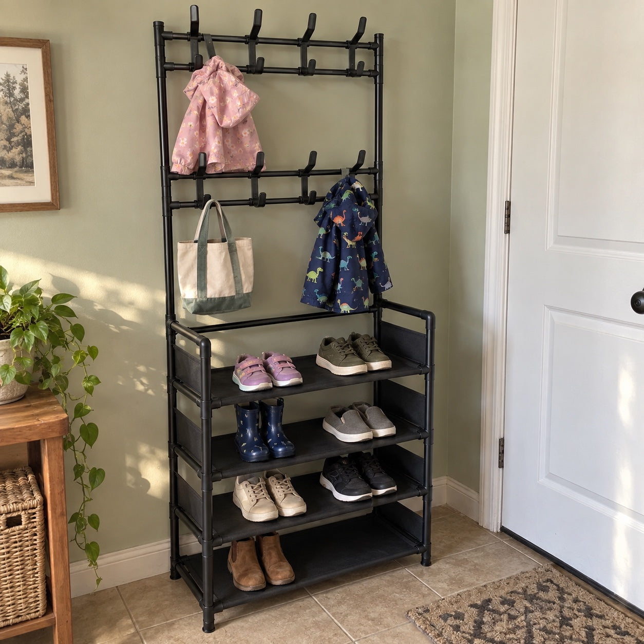 the black rack in a sage-walled family entryway, holding children's rain jackets, a canvas tote, and children's and adult shoes and boots.