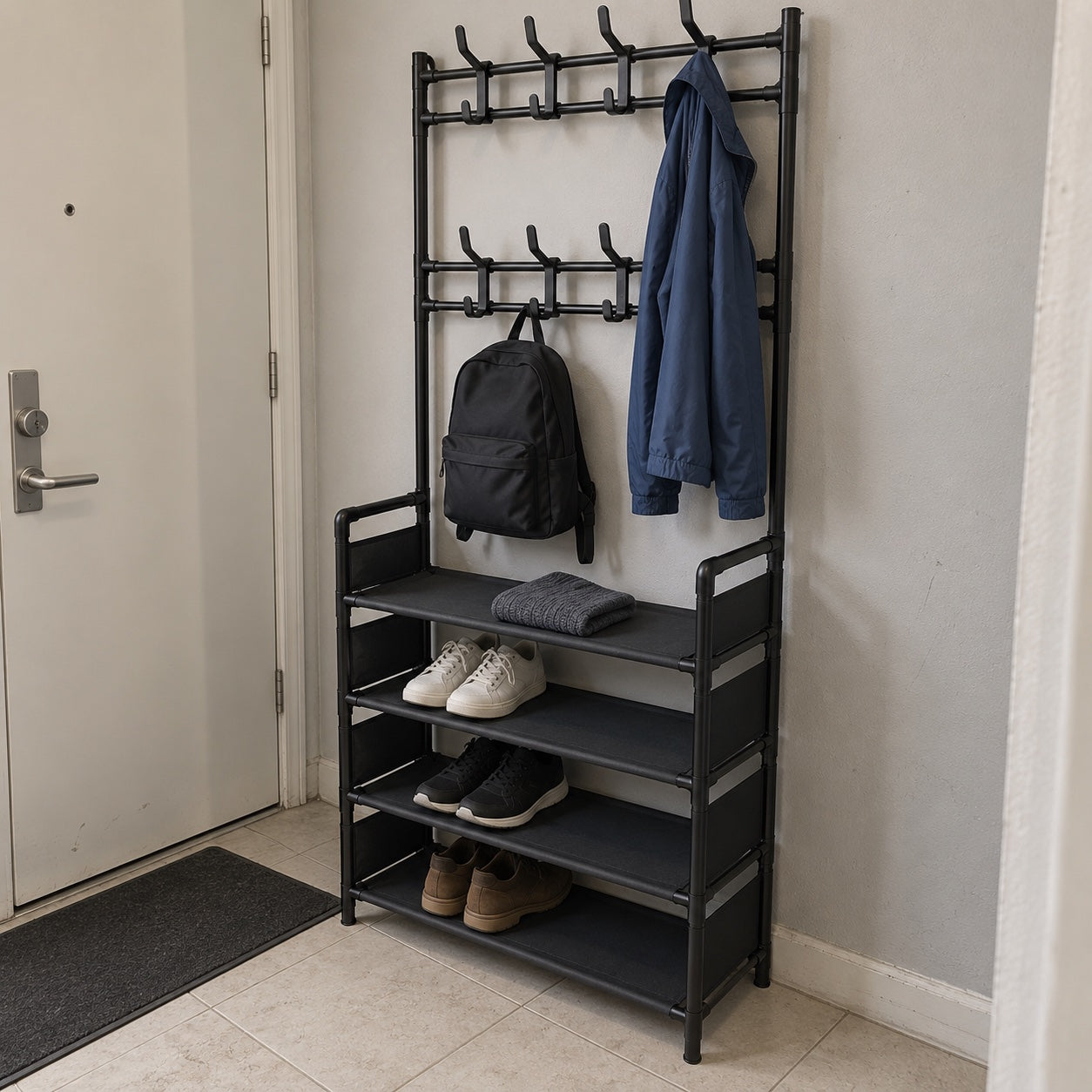 the black rack beside an entrance door in a narrow hallway, with a blue jacket, black backpack, folded grey knit and shoes.