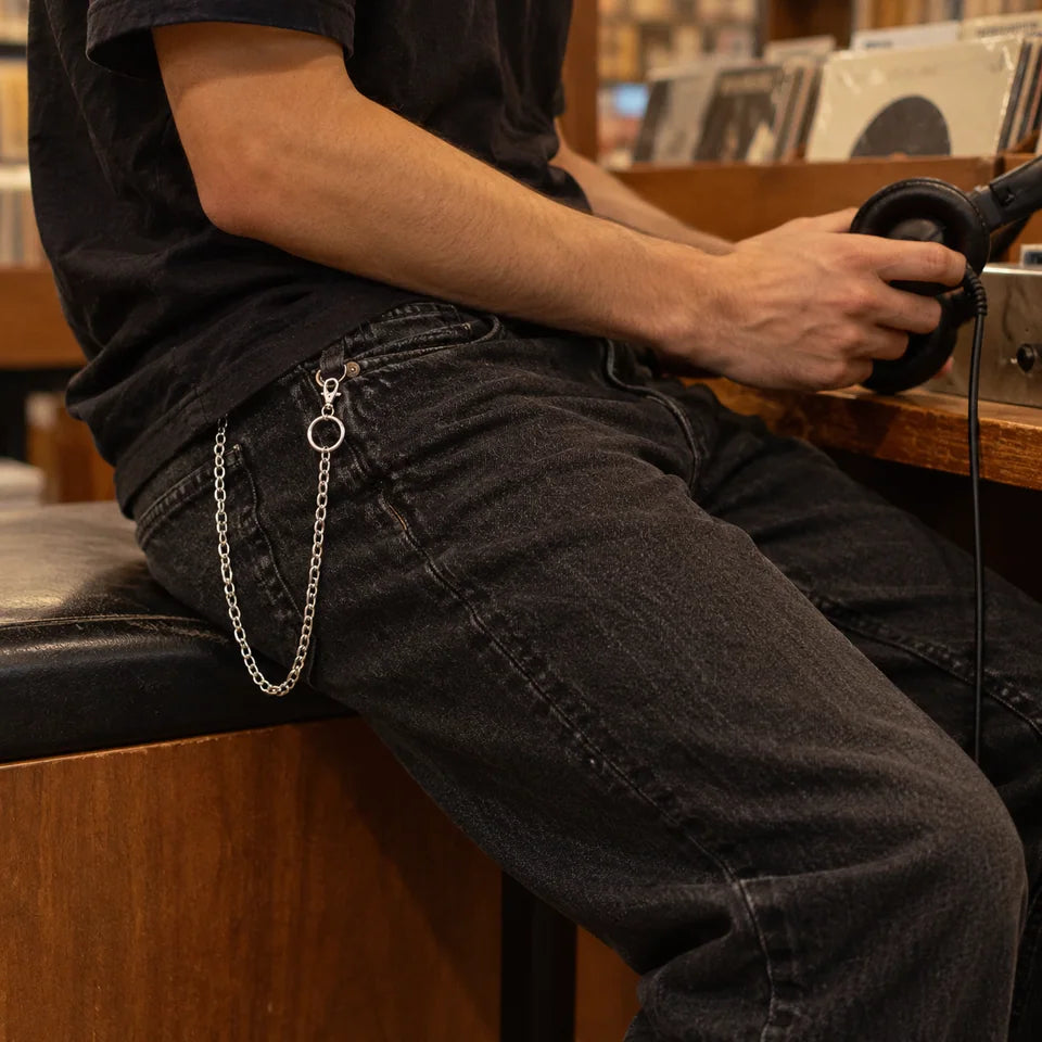 Adult in black jeans with single-strand chain at a listening booth