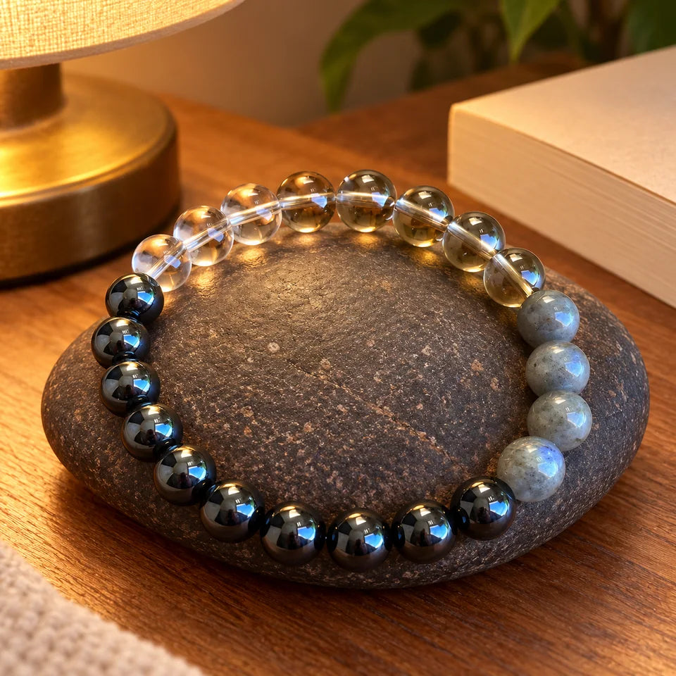 Grounding style bracelet on a dark stone beside a bedside book and lamp.