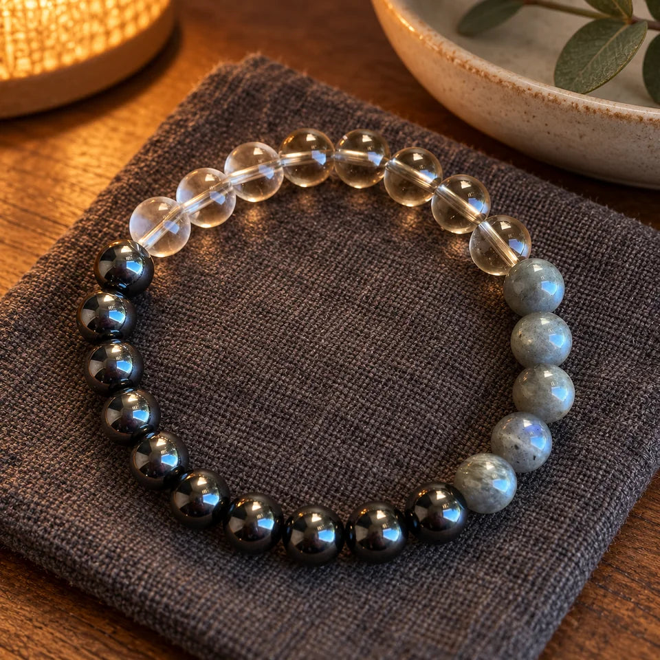 Grounding bracelet resting on charcoal linen beside a ceramic dish in warm lamplight.