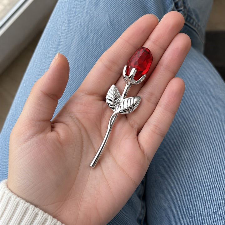 Ruby and silver rose in a palm above blue jeans.