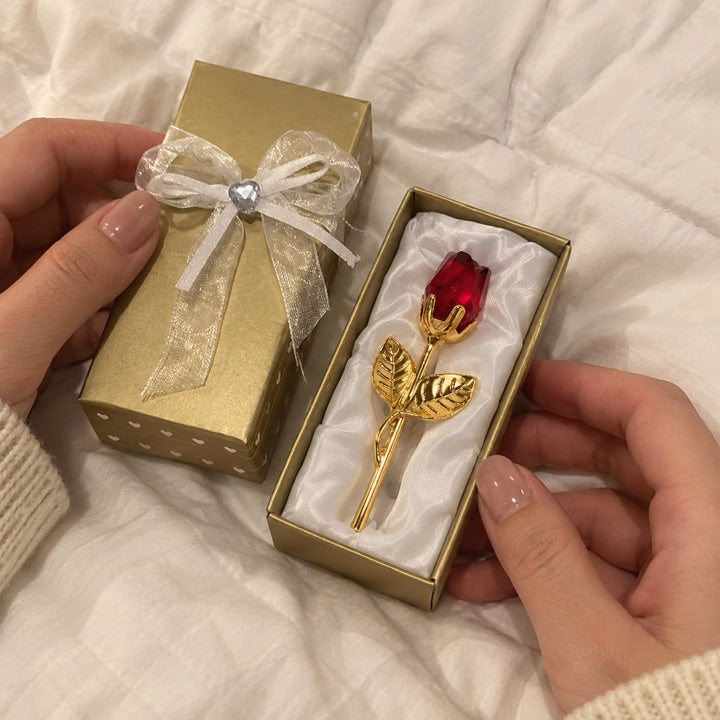 Ruby and gold rose in its open gift box on a duvet.