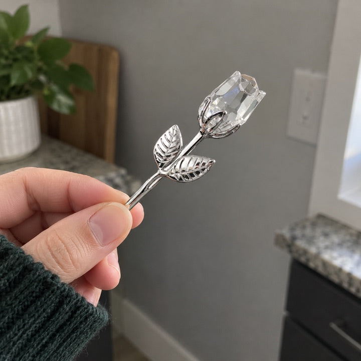 Clear and silver rose held by its stem.