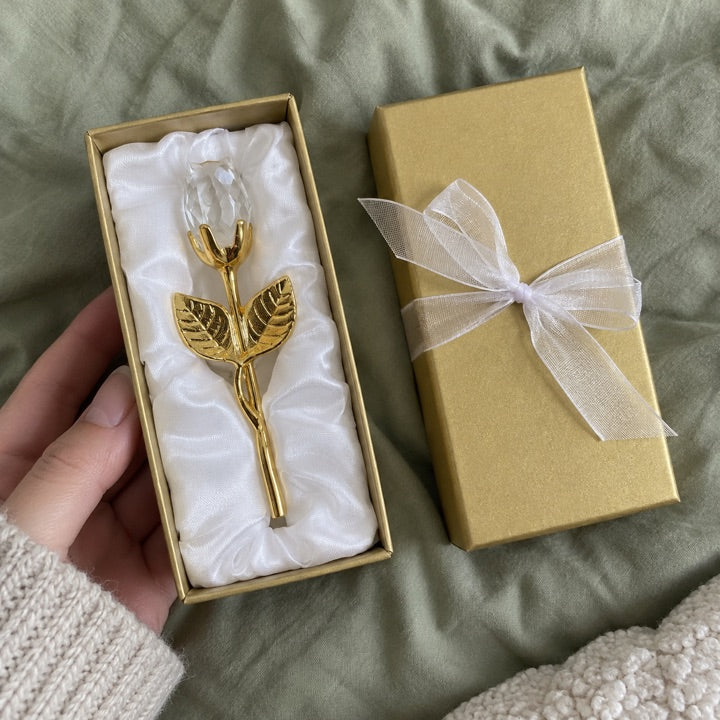 Clear and gold rose gift on a sage-green duvet.