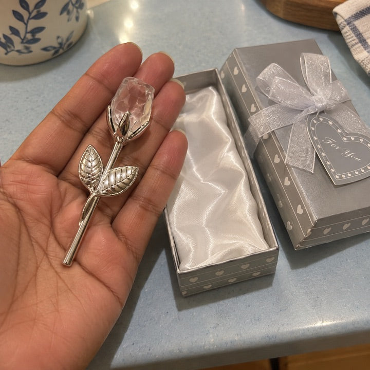 Clear and silver rose in a hand beside its box.
